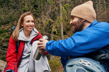 Bir adam ormanda kadınla çay termosunu paylaşıyor.
