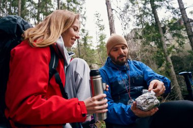 Ormandaki kadının yanındaki folyodan yemek çıkaran yürüyüşçü.