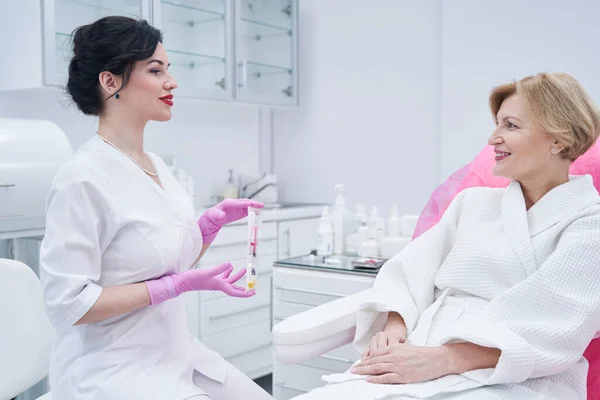 Beautician showing cosmetic syringe to woman in beauty salon — Fotografia de Stock