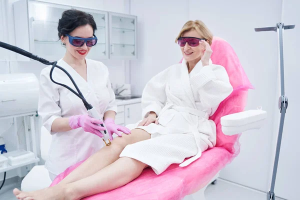 Esteticista alegre usando dispositivo de depilación láser en salón de belleza — Foto de Stock
