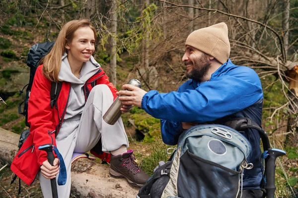 Walking tourists on tree trunk sharing tea with each other — Stock Photo, Image