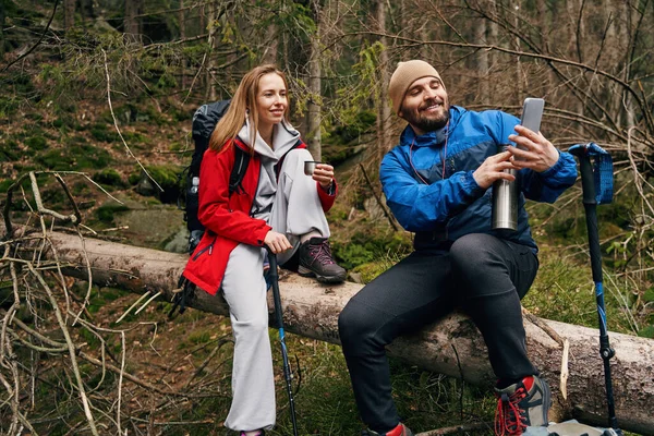 Termoslu bir adam akıllı telefondan dışarıdaki kadınlara fotoğraf gösteriyor.