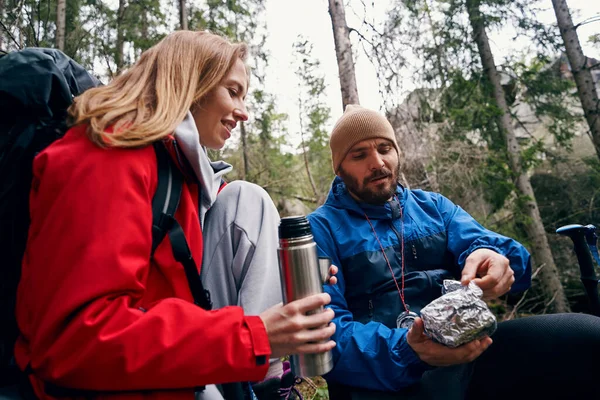 Ormandaki kadının yanındaki folyodan yemek çıkaran yürüyüşçü.