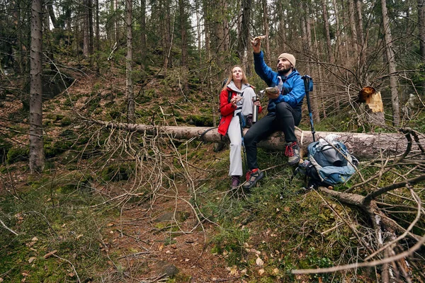 Açık havada ağaç gövdesinde sandviç yiyen iki turist.