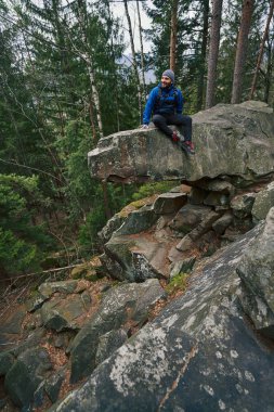 Sırt çantalı, arka planda ormanla birlikte uçurumun kenarında dinleniyor.