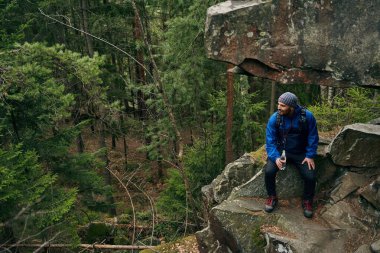 Sırt çantasında su şişesiyle kayanın altında oturan