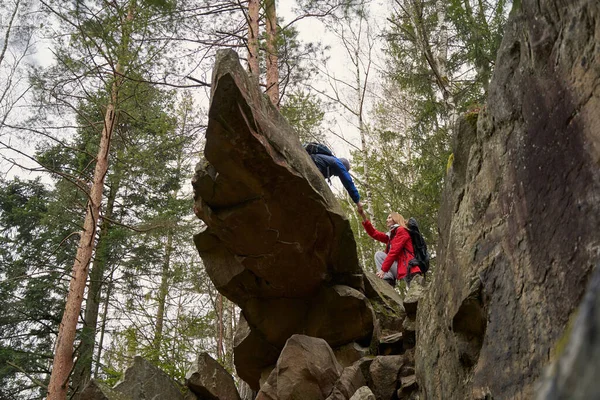 Женщина-туристка помогает мужчине спуститься со скалы — стоковое фото