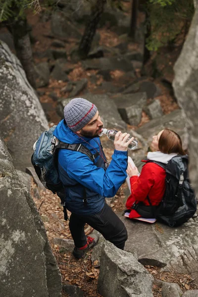 Erkek yürüyüşçü kayalıklardaki şişeden su içiyor.
