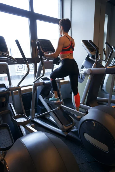 Sporty lady exercising on cross-trainer at gym