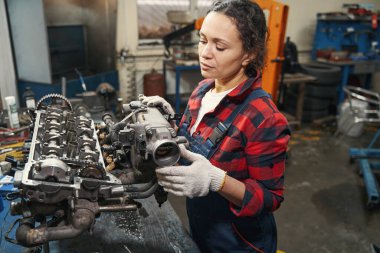 İş eldivenli kadın araç teknisyeni tamir istasyonunda otomobil motoru tamir ediyor.