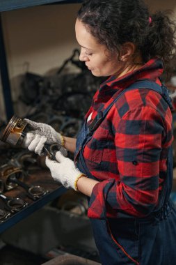 Tamir istasyonunda çalışırken metal otomobil parçası tutan iş eldivenli kadın teknisyen.