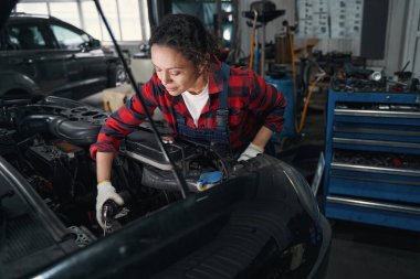 İş eldivenli kadın araç teknisyeni tamir istasyonunda otomobil motoru tamir ediyor.