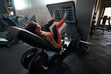 Spor salonundaki direniş eğitimi sırasında bacak egzersizi yapan bayan sporcu.