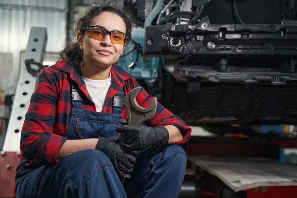 妇女汽车技师手持金属工具 在汽车维修车库摆姿势时看着相机 — 图库照片