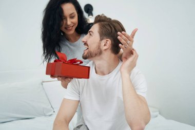 Gülümseyen genç bayan yatakta oturan neşeli adama hediyesini sunuyor.