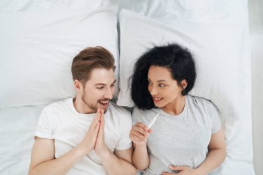 Gülümseyen mutlu adam hamilelik testine genç bir kadının ellerinde bakıyor.