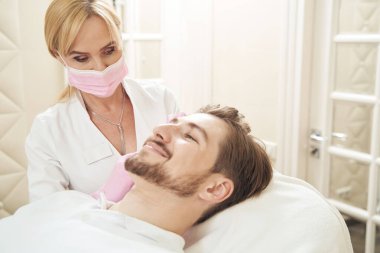 Botulinum toksini enjekte edilirken ameliyat yatağında uzanan heyecanlı adam.