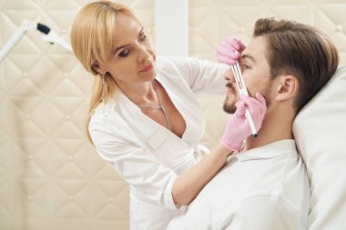 Beyaz kadın güzellik uzmanı. Güzellik prosedürü için erkek yüzüne işaretler çiziyor.