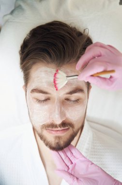 Yüz maskesi takılan erkek yüzünün üst görüntüsü ve fırçadan kafasına krem bulaşması.