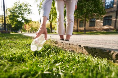 Kafası kesilmiş bir kadın eli, yürürken çimenlikten plastik bir kap su alıyor.