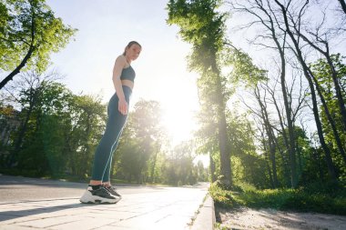 Açık havada antrenman yaparken spor giyim bölümünde ayakta duran atletik gülümseyen kadın portresi.