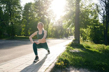 Gülümseyen genç kadın güneşli bir günde yeşil şehir sokağında antrenman yaparken hamleler yapıyor.