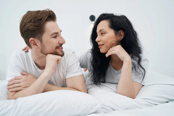Loving female lying in bed next to her smiling pleased life partner