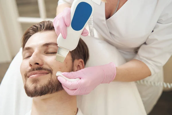 超音波スクラバーで男性の顔の毛穴から汚れや細胞の破片を除去する美容師 — ストック写真