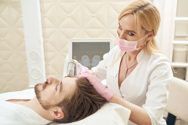 Kvinnlig Kosmetolog Drar Huden Manligt Huvud Med Smas Ansiktslyftningsmaskin Skönhetscenter — Stockfoto