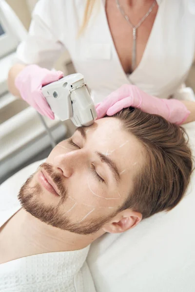 リラックスした男の顔に超音波皮膚引き締めを行う美容師 クリームで覆われて — ストック写真