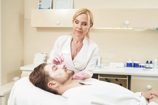 男性の顔の治療のためのクリームを適用審美的な医療センターの女性の美しさの専門家 — ストック写真