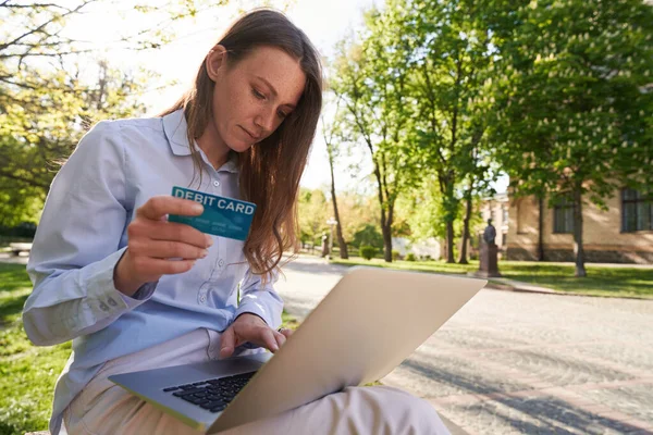 Kobieta Używa Laptopa Trzyma Kartę Bankową Patrząc Ekran Siedząc Zielonej — Zdjęcie stockowe