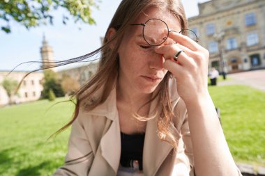 Bitkin düşmüş dişi, teneffüs sırasında yemyeşil bir bankta otururken kadınlarını tutuyor.