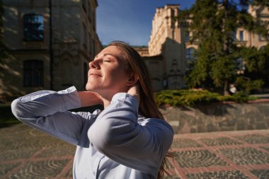 Gülümseyen genç bir dişi eski şehirde yürüyor ve gözlerini kapıyor. Meydanda güneşlenirken.