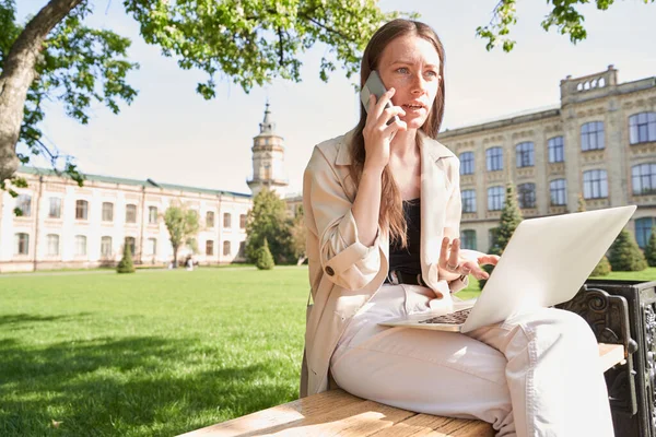 Niski Kąt Inteligentnej Bizneswoman Siedzi Ławce Parku Notebooka Mówi Smartfonie — Zdjęcie stockowe