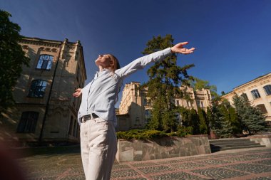 Düşük açılı mutlu kadın gözleri kapalı ve kollarını gökyüzüne uzatarak eski şehirde sıcak bir günün tadını çıkarıyor.