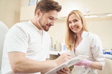 Neşeli kadın güzellik işçisi, panoyu belgeyle desteklerken bir yandan da erkek imzasını atıyor.