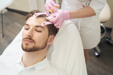 Güzellik uzmanı erkek kafasına kırışıklık aldırmak için botulinyum toksin enjekte ediyor.