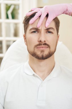 Güzellik uzmanının eli enjeksiyon işleminden önce insan alnını burun köprüsünün üstüne katlıyor.