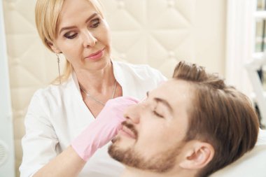 Güzellik salonu çalışanı erkek müşteriye iğne yaparken dikkatli davranır.