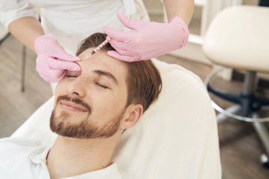Kozmetolojist, estetik tıp merkezindeki şırıngadan erkek kafasına yaşlanma önleyici serum enjekte ediyor.