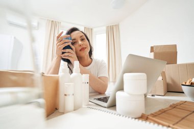 Karton kutular ve kozmetik ürünlerin arasında oturmuş gülümseyen mutlu kadın.