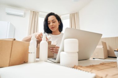 Kozmetik ürünleri karton kutunun içine yerleştiren konsantre olmuş online mağaza çalışanı.