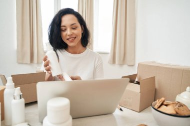 Gülümseyen çevrimiçi mağaza çalışanı dizüstü bilgisayarda müşteriye cilt ürünlerini gösteriyor.