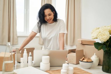 Gülümseyen internet işçisi masaya eğilip dizüstü bilgisayara bakıyor.