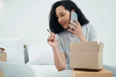 Neşeli kadın telefon konuşması sırasında dizüstü bilgisayara bakıyor.