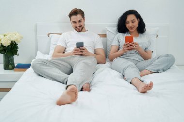 Yatakta uzanmış ellerinde cep telefonlarına bakan genç bir çift.