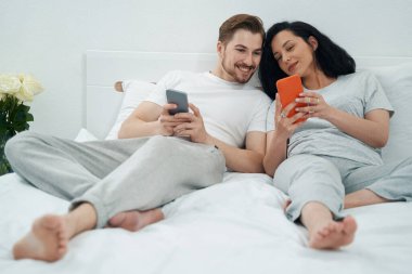 Gülümseyen neşeli arkadaşına cep telefonuyla bir şey gösteren genç bir kadın.