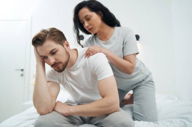 Değer veren genç bir kadın yatakta oturan üzgün bir erkeğe yaslanıyor ve ona rahatlatıcı bir masaj yapıyor.