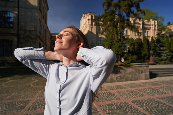 Mutlu çilli kadın, güzel binanın yakınındaki meydanda duruyor ve kapalı gözlerle sıcak havanın tadını çıkarıyor.